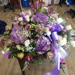 Large bouquet of purple hydrangeas, roses, and white flowers with a lavender ribbon