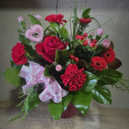 Red roses and carnations in a pink vase with a heart decoration and ribbon