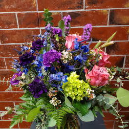 Mixed bouquet of pink, purple, and blue flowers in a glass vase