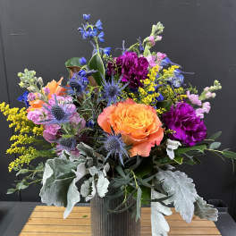 Colorful bouquet in a ribbed metal vase with orange and purple blooms