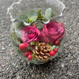 Two magenta roses in a clear glass vase with a pinecone and red berries