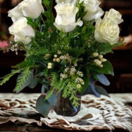 White roses arranged in a glass vase with greenery