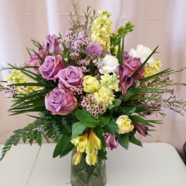 Lavender roses and yellow flowers arranged in a glass vase