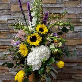 Tall mixed bouquet with sunflowers, white hydrangea, and purple spikes in a glass vase