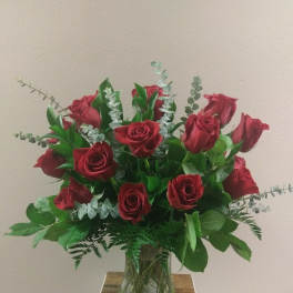 Red roses arranged in a clear glass vase with eucalyptus and greenery