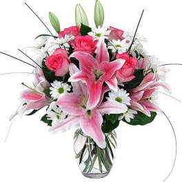 Pink lilies and roses arranged in a clear glass vase with white daisies