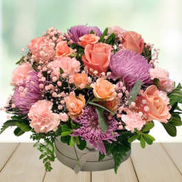 Pink and purple mixed flower arrangement in a round box