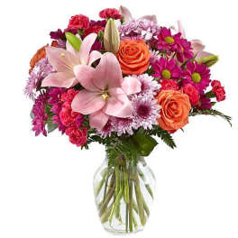 Mixed bouquet of pink lilies, roses, and daisies in a clear glass vase