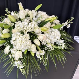 White floral casket spray with roses, lilies, and hydrangeas