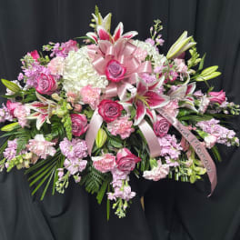 Pink and white floral spray with lilies, roses, and ribbon on a black backdrop