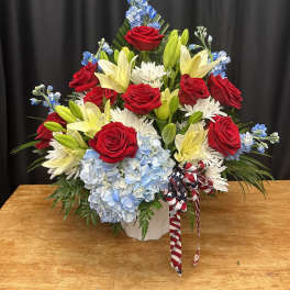 Red roses, yellow lilies, and blue hydrangeas in a white vase