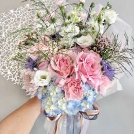 Handheld bouquet of pink and white roses with blue hydrangeas