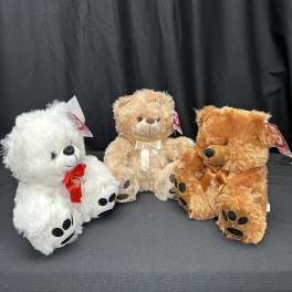 Three teddy bears with ribbons sitting on a dark surface