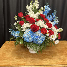 Red roses, blue hydrangeas, and white daisies in a white vase