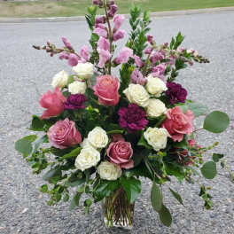 Pink and white roses with purple blooms in a clear glass vase