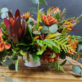 Orange and burgundy floral arrangement in a white vase