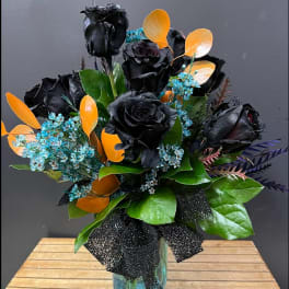Black roses in a glass vase with orange leaves and blue filler flowers