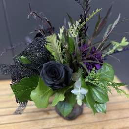 Black rose arrangement with purple accents in a small vase