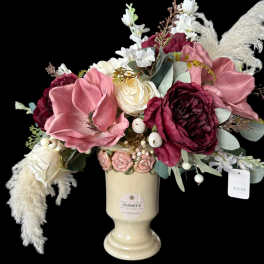 Pink and burgundy flowers arranged in a cream vase with white feathers.