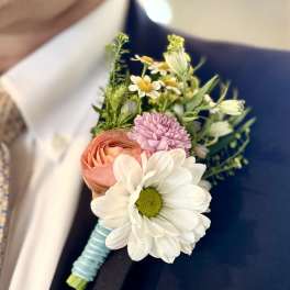 Boutonniere with white daisy, peach ranunculus, and pink bloom