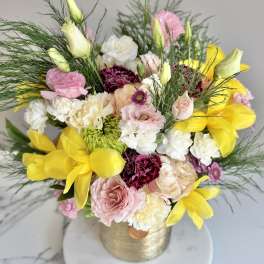 Arrangement of yellow tulips, pink roses, carnations, and white blooms in a gold vase