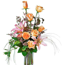 Tall bouquet of peach roses and pink lilies in a glass vase