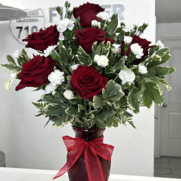 Arrangement of red roses and small white flowers in a red glass vase with a bow.