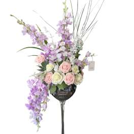Tall floral arrangement in a wine glass-shaped vase with pink and lavender blooms