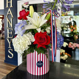 Mixed bouquet with lilies, roses, hydrangeas, and agapanthus in a striped box