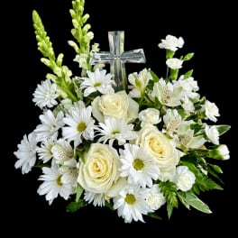 White floral arrangement with roses, daisies, and a clear glass cross