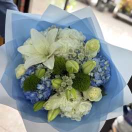 Bouquet of white lilies, blue hydrangeas, and pale roses wrapped in blue paper
