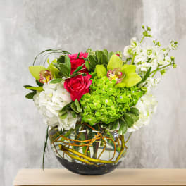 Bouquet of pink roses, green orchids, and white blooms in a glass vase
