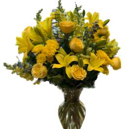 Yellow lilies and roses arranged in a clear glass vase