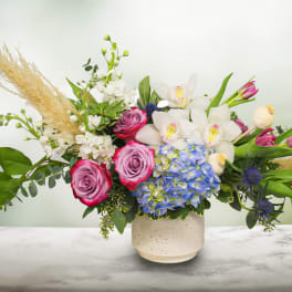 Mixed bouquet with pink roses, white orchids, and blue hydrangea in a ceramic vase