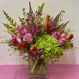 Pink roses and red tulips arranged with green hydrangea in a glass vase.