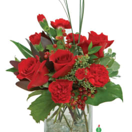 Compact red rose and carnation arrangement with tall grass in a clear square glass vase