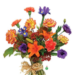 Bright mixed bouquet of orange lilies, purple irises, and assorted blooms in a clear glass vase