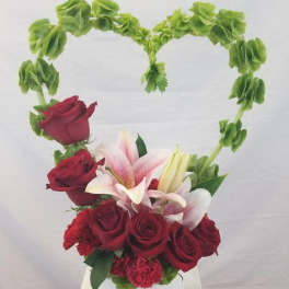Heart-shaped floral arrangement with red roses and pink lilies in a white container