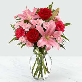Pink lilies, red roses, and carnations in a clear glass vase