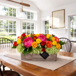 Bright mixed flower arrangement in a wooden box on a dining table