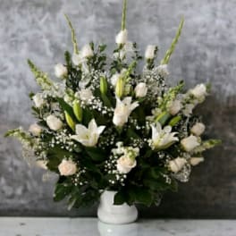 White floral arrangement in a white vase with lilies and roses