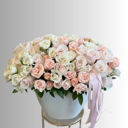 Large bouquet of pale pink and white roses in a white vase with a pink ribbon
