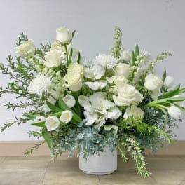 White floral arrangement in a white vase with roses and mixed blooms