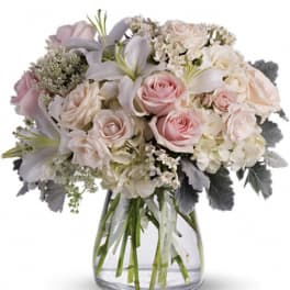 Pink and white roses with lilies in a clear glass vase