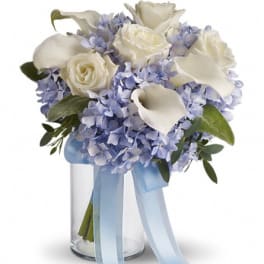 White roses and calla lilies in a glass vase with a blue ribbon