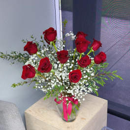 Red roses arranged in a clear glass vase with white baby's breath