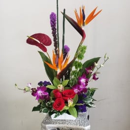 Tropical flower arrangement with red roses and purple orchids in a decorative vase