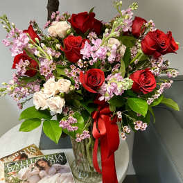 Red and blush rose bouquet in a glass vase with a red ribbon