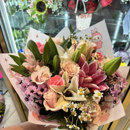 Handheld bouquet of pink roses, lilies, and daisies in pastel wrap