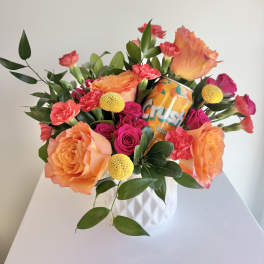 Orange and pink flower arrangement in a white vase with a soda can